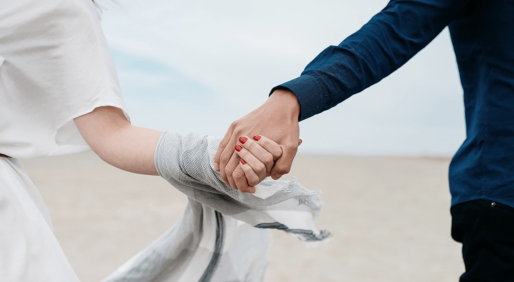 Para trzymająca się za dłonie na tle piasku i morza